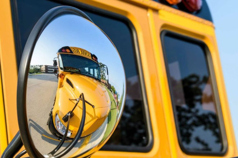 Mirror on a school bus, showing another bus.