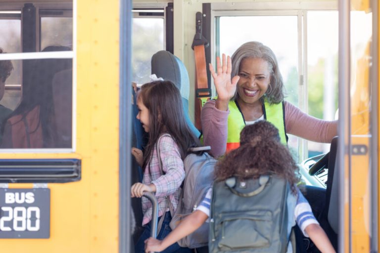 Bus driver waving hello to students.