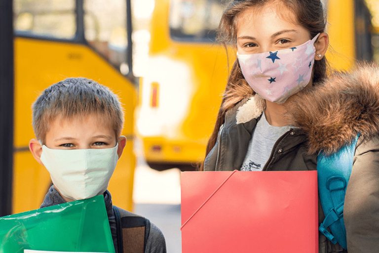 Kids in front of a school bus, wearing Covid masks