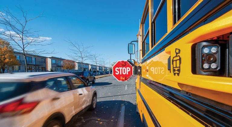 View of a school bus stop-arm down with a car speeding past it on the left